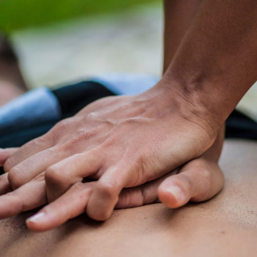 A person performing CPR with both hands pressing on another person's chest. The background is blurred, highlighting the focus on the hands and chest area.