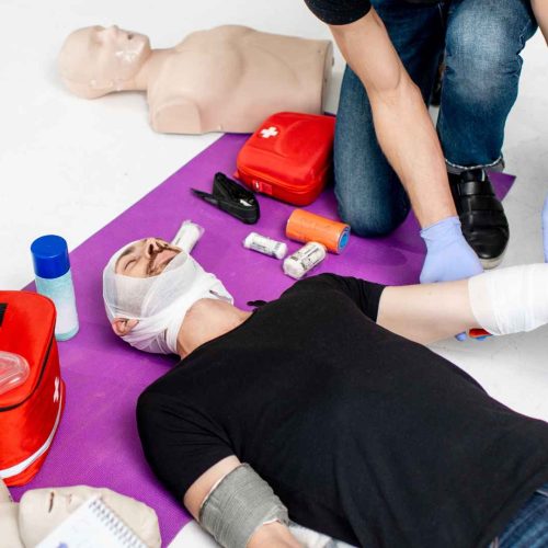 Group of first aid students practicing bandaging and wound care skills with a CPR manikin and first aid kit during a training course
