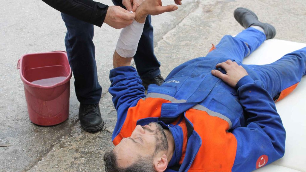 man in a worker's uniform laying on the ground while another man is bandaging his arm