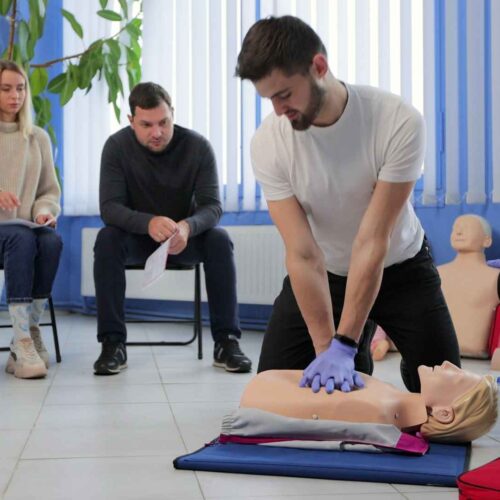 CPR course with a student performing CPR technique on a mannequin and other students and instructor overseeing