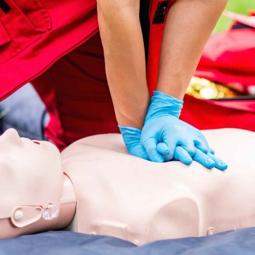 close up of a person wearing nitrile gloves and performing cpr on a manikin outside