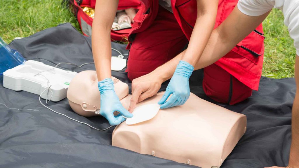 close up of someone placing AED pads on a CPR manikin and another person pointing where they should be placed