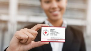 A person in a suit holds up a Red Cross certification card. The card includes details such as the name "Jack Harlow," certification number, start and end dates, and a CPR/AED for Professional Rescuers and First Aid credential.