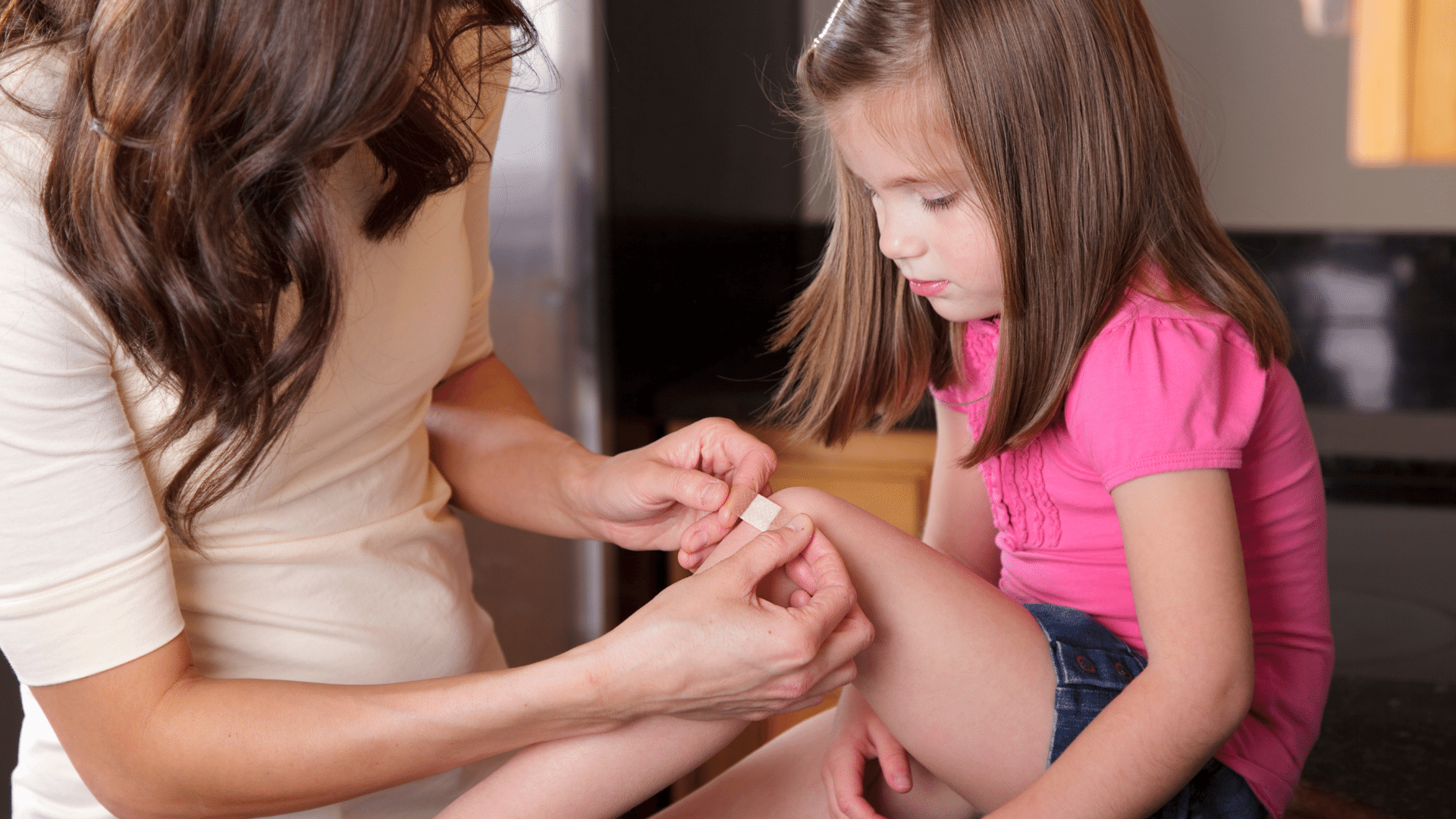 Woman applying bandage on a girl's knee.