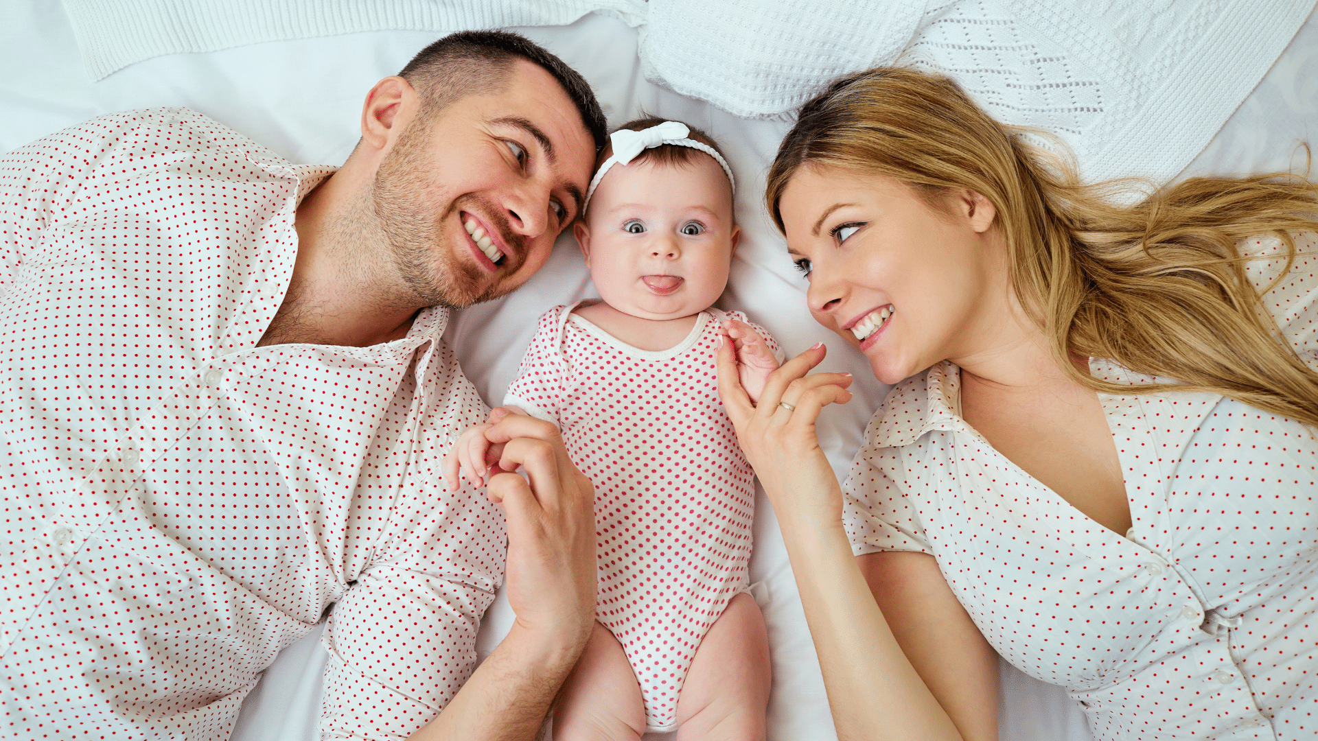 Happy parents laying in bed with their baby.