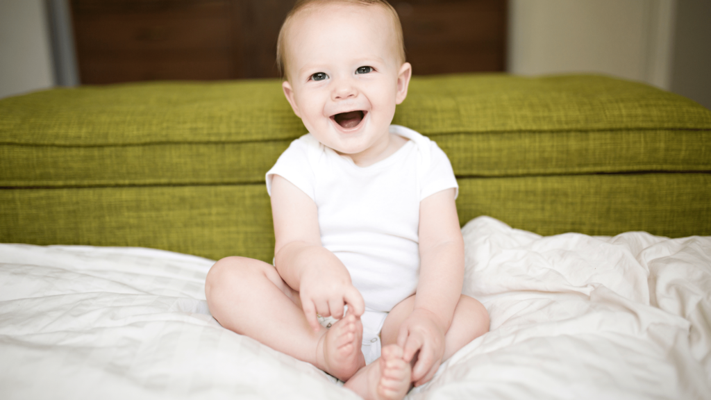 smiling baby sitting on a bed.