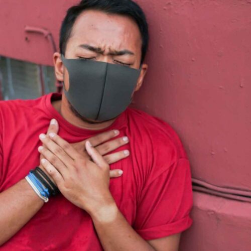 Person experiencing respiratory distress after inhaling chemicals, holding chest while sitting outdoors on the ground