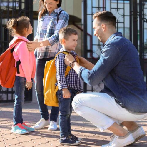 Parents preparing their children wearing backpacks going back to school.