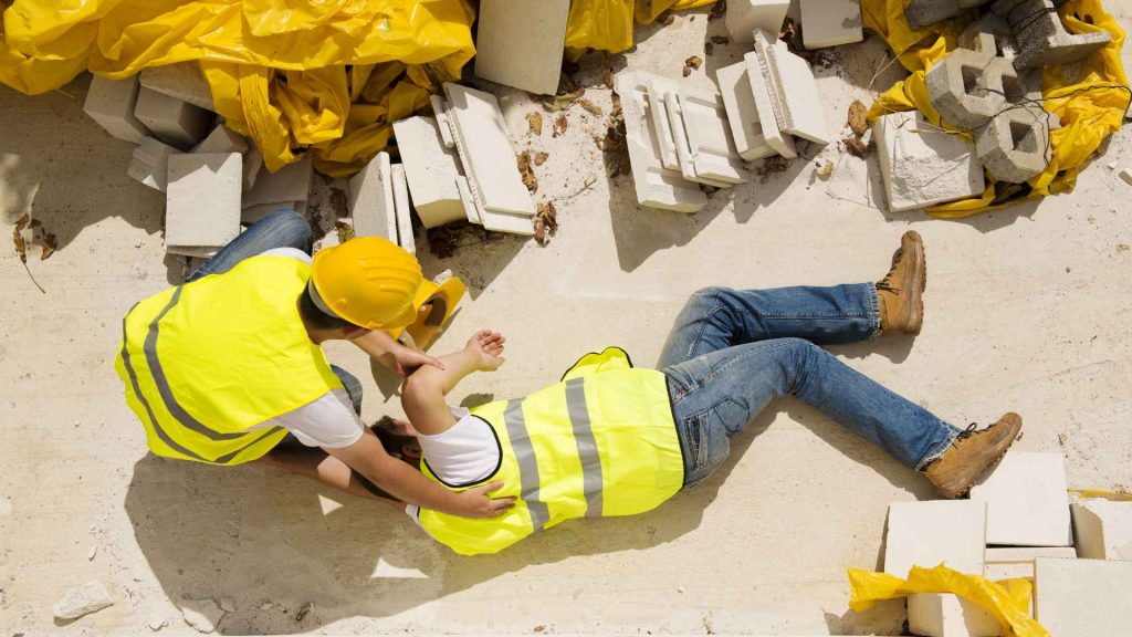 aerial view of one construction worker laying on his side on the ground and another construction worker trying to help him