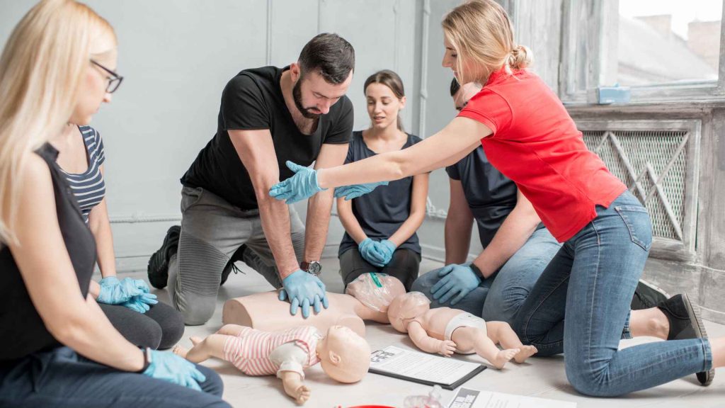 a first aid and cpr training of men and women. a man is practicing cpr on a manikin and a female instructor is guiding him