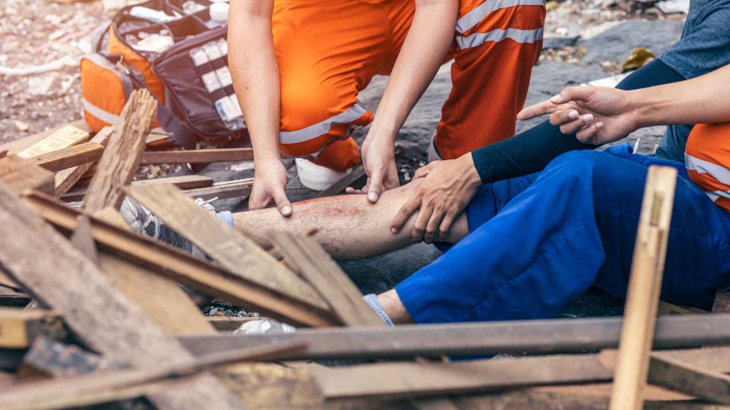 close up of a person's leg injured from fallen wood around him. another person is examining his leg which looks badly scratched