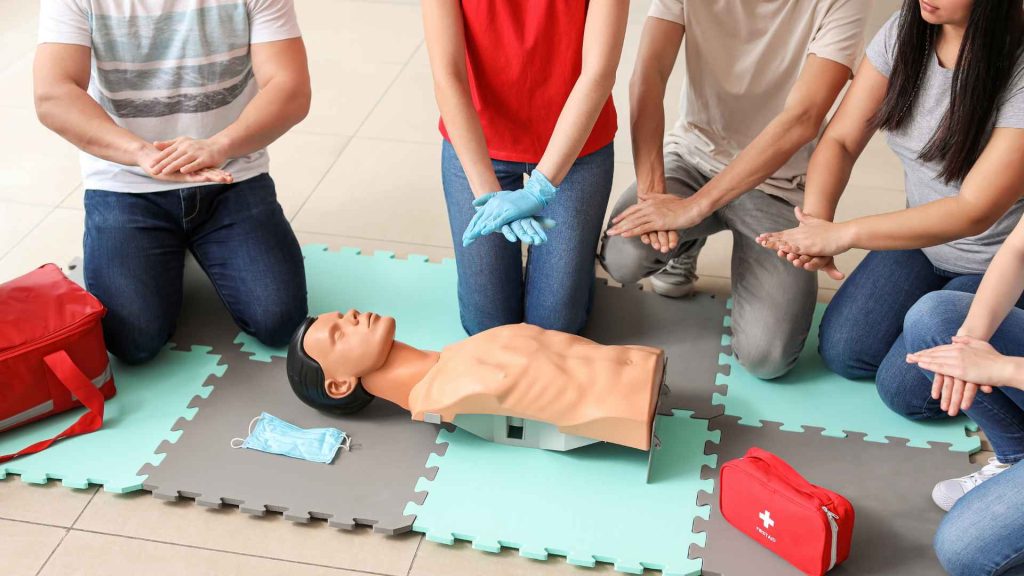 a close up of a small group of people learning how to place their hands on a manikin to perform cpr