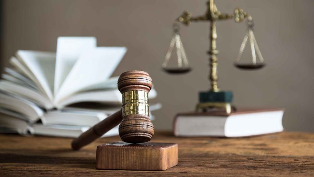 close up of court room items such as a gavel, balance scale, and books.