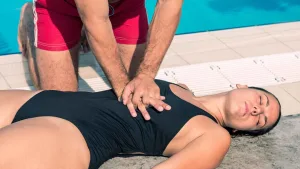 Lifeguard performing chest compression CPR on a cardiac arrest victim beside a swimming pool, demonstrating lifeguard first aid certification skills