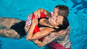 Lifeguard performing an in-water rescue by supporting a swimmer from behind using a rescue buoy, demonstrating lifesaving first aid skills