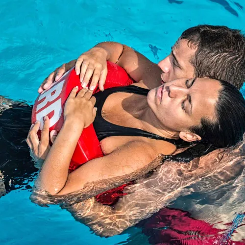Male lifeguard in pool holding an unconscious woman afloat and bringing her to safety